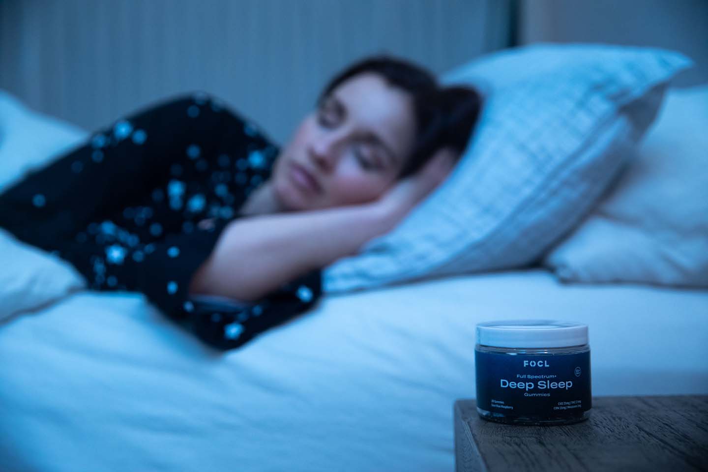 Blue jar of CD gummies on a nightstand with a woman sleeping in the background
