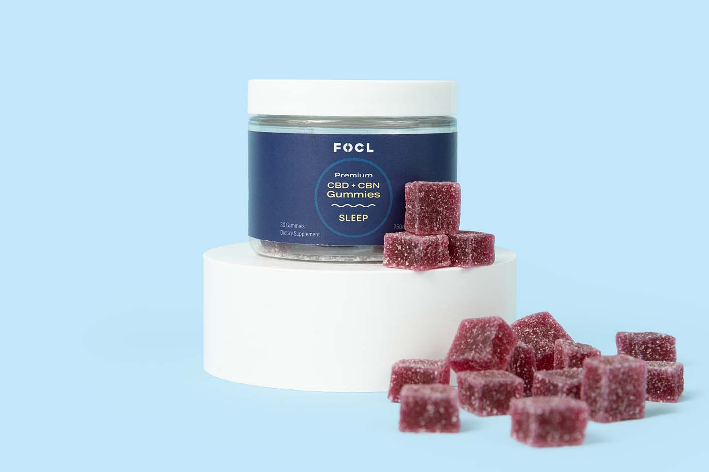 purple CBD gummies next to a blue jar of FOCL CBD Plus CBN Sleep Gummies on a white stand