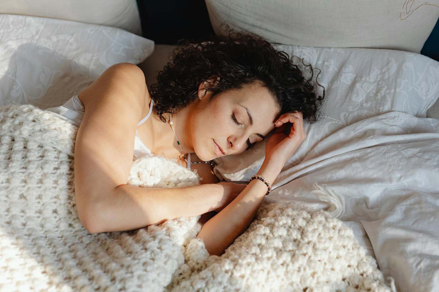 a woman peacefully sleeping on bed underneath knitted white blanket