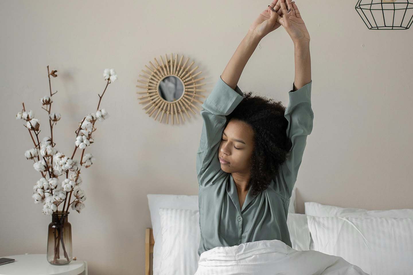 a woman sitting on bed waking up as she strech her arms up high