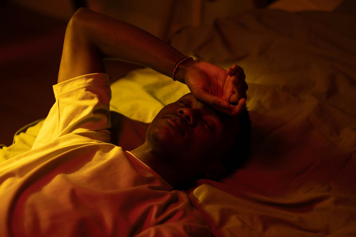 a man lying on a bed at night with his right hand placed on his forehead