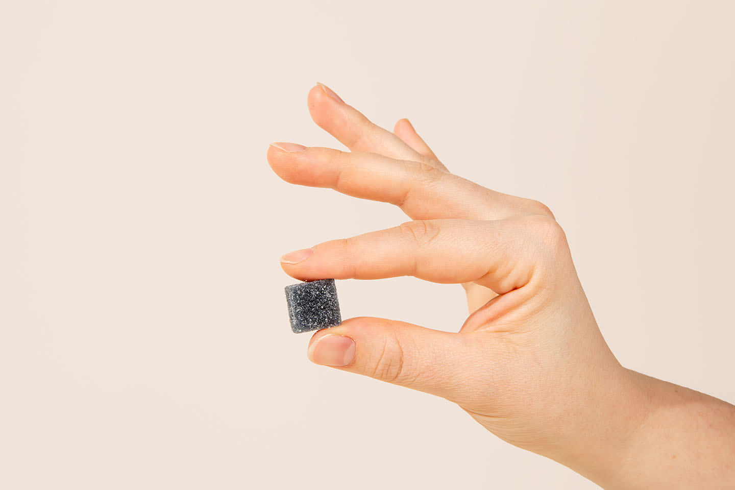 a right hand holding a dark blue CBD gummy between thumb and forefinger