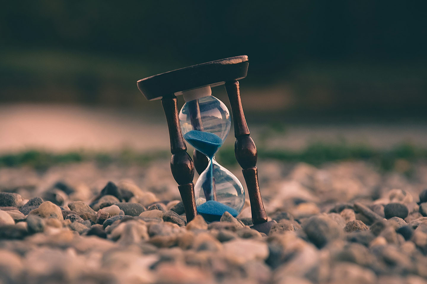 a clear hourglass with blue sand on stones