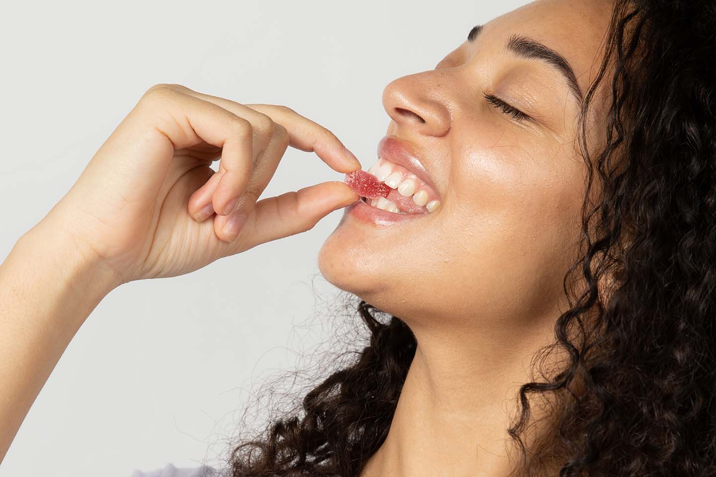 a woman smiling while biting a red-colored gummy