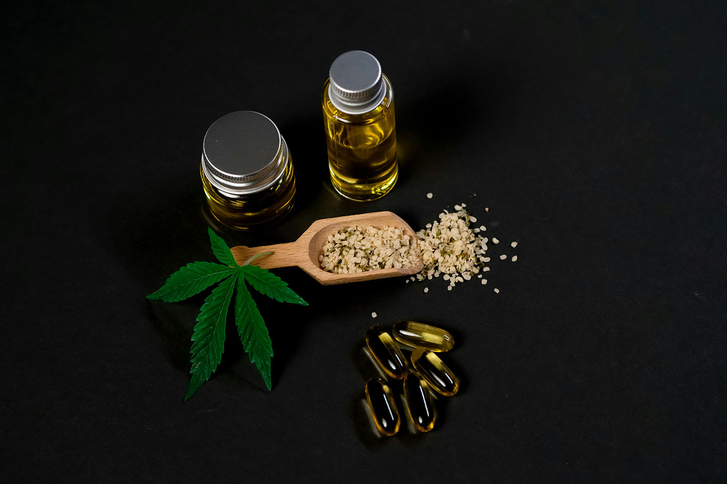 Leaf next to jars of oil, yellow capsules, and wooden scoop full of seeds