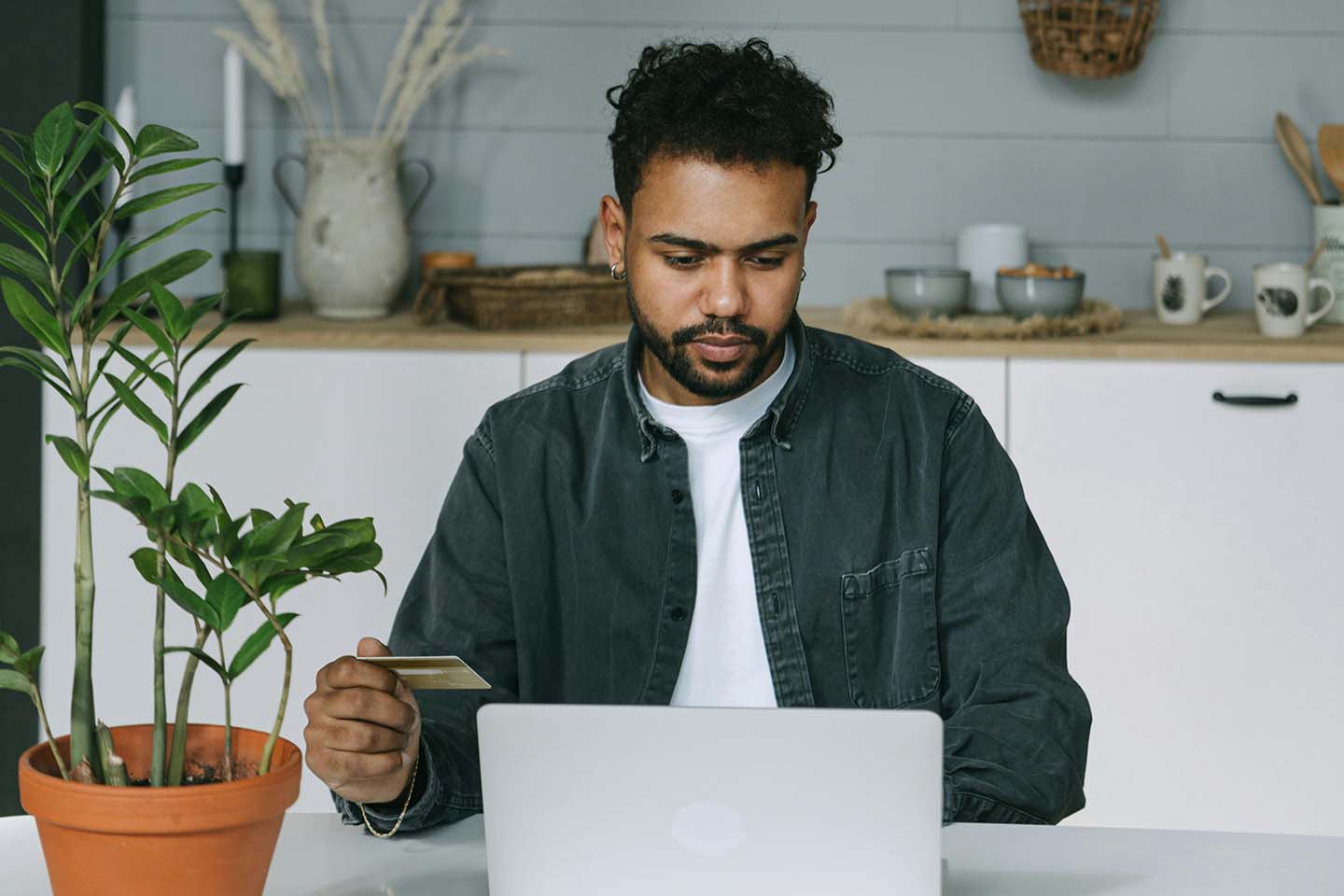 a man sitting on a table and using a laptop while holding a credit card