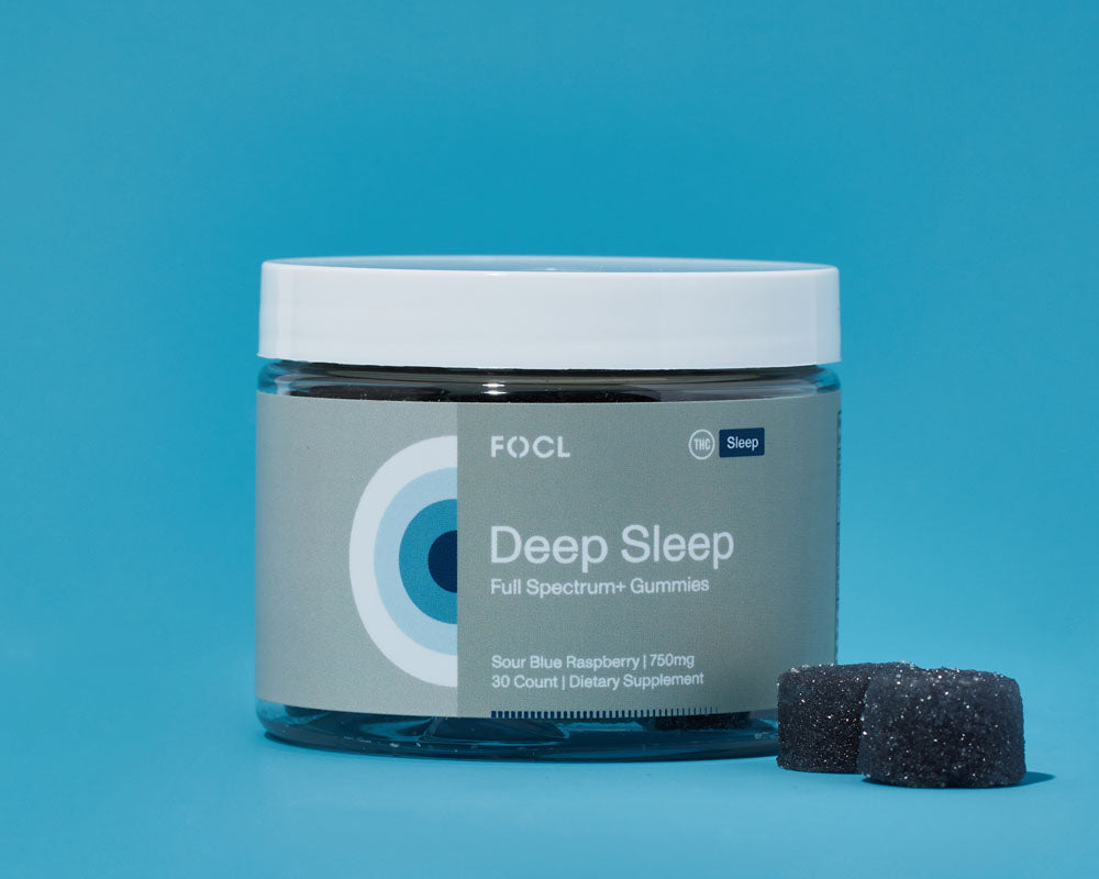jar of FOCL Deep Sleep gummies beside two dark blue gummies
