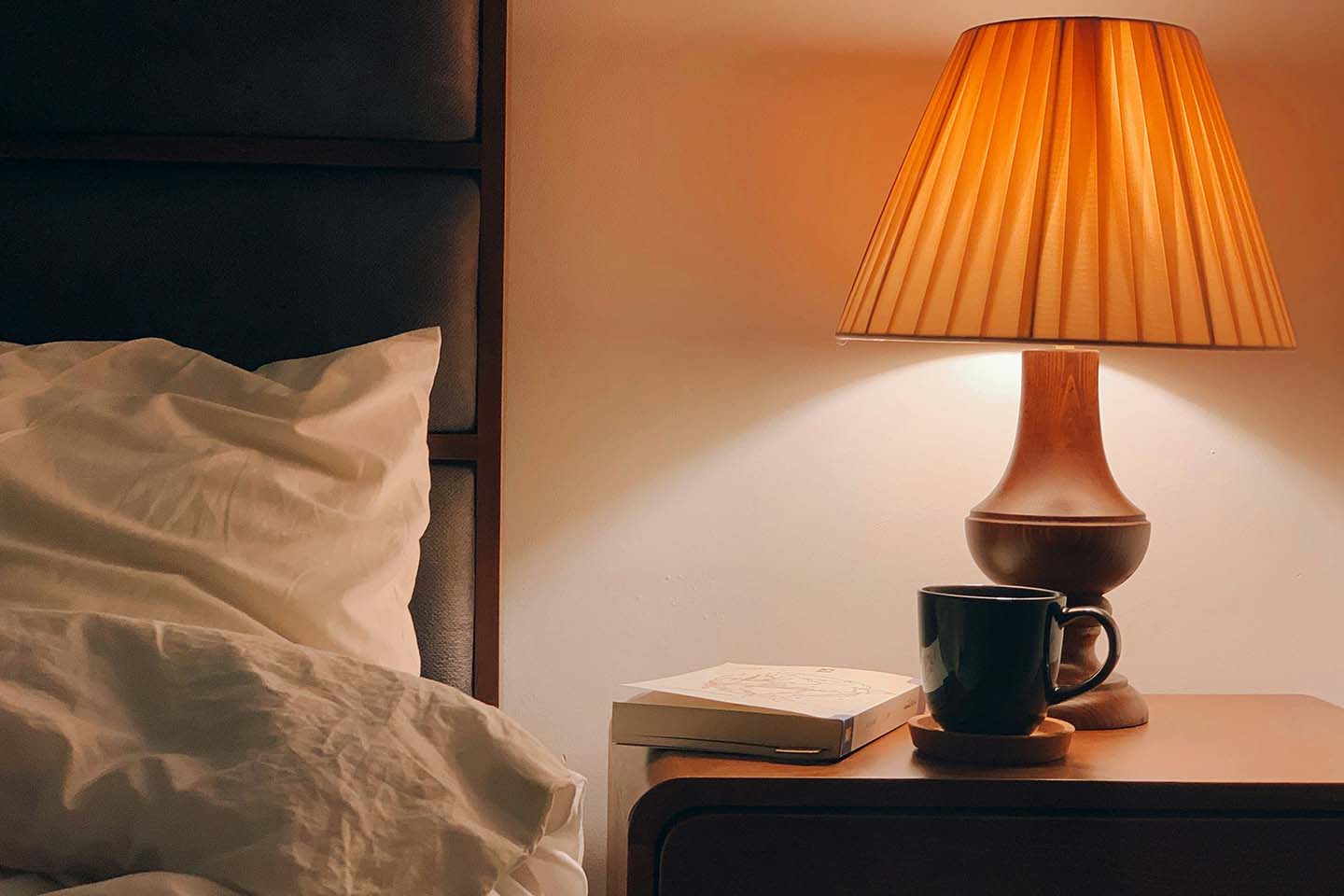 Bed with white sheets and a bedside table with a lighted lamp.