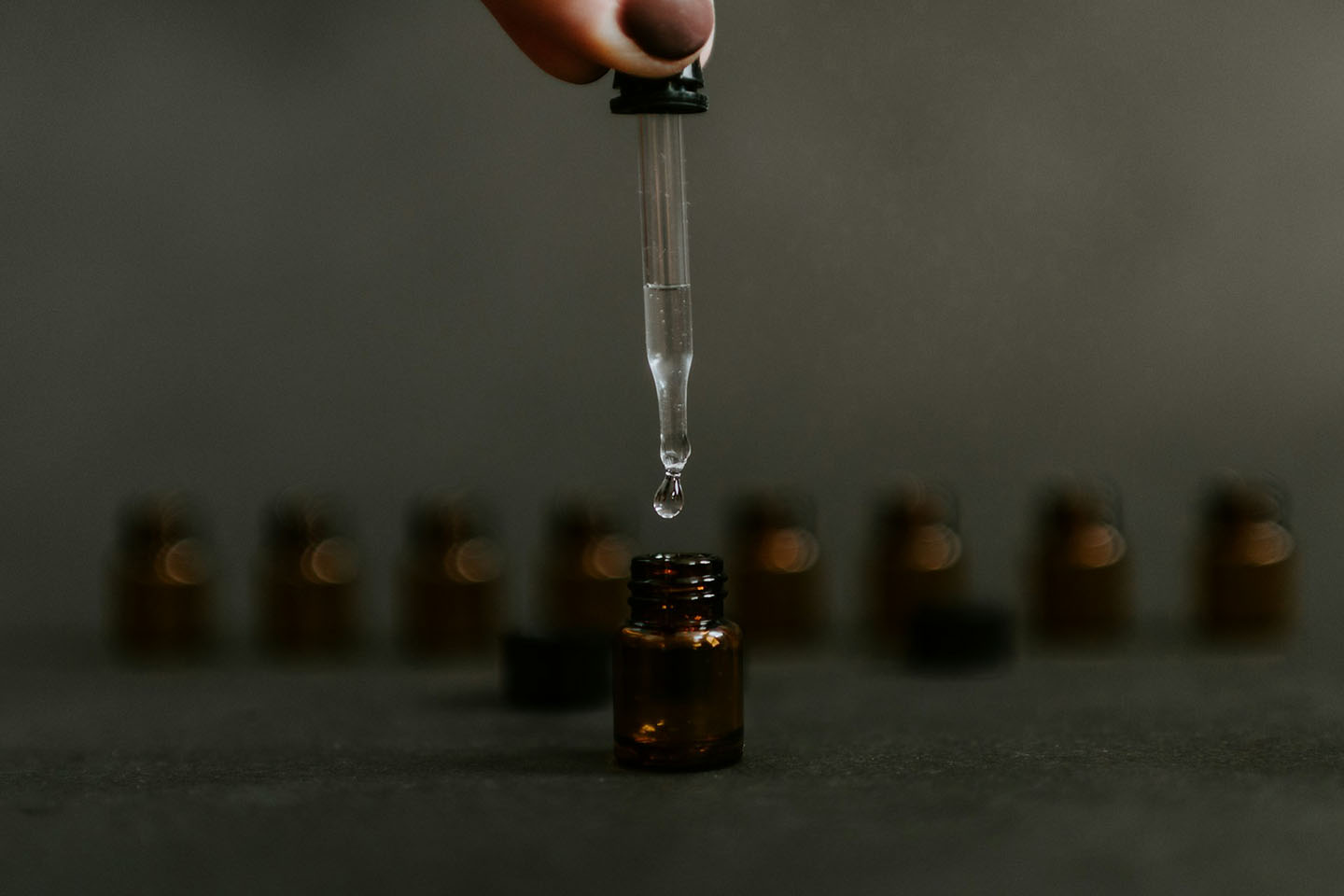 Closeup of a dropper of oil being squeezed into a small brown jar.