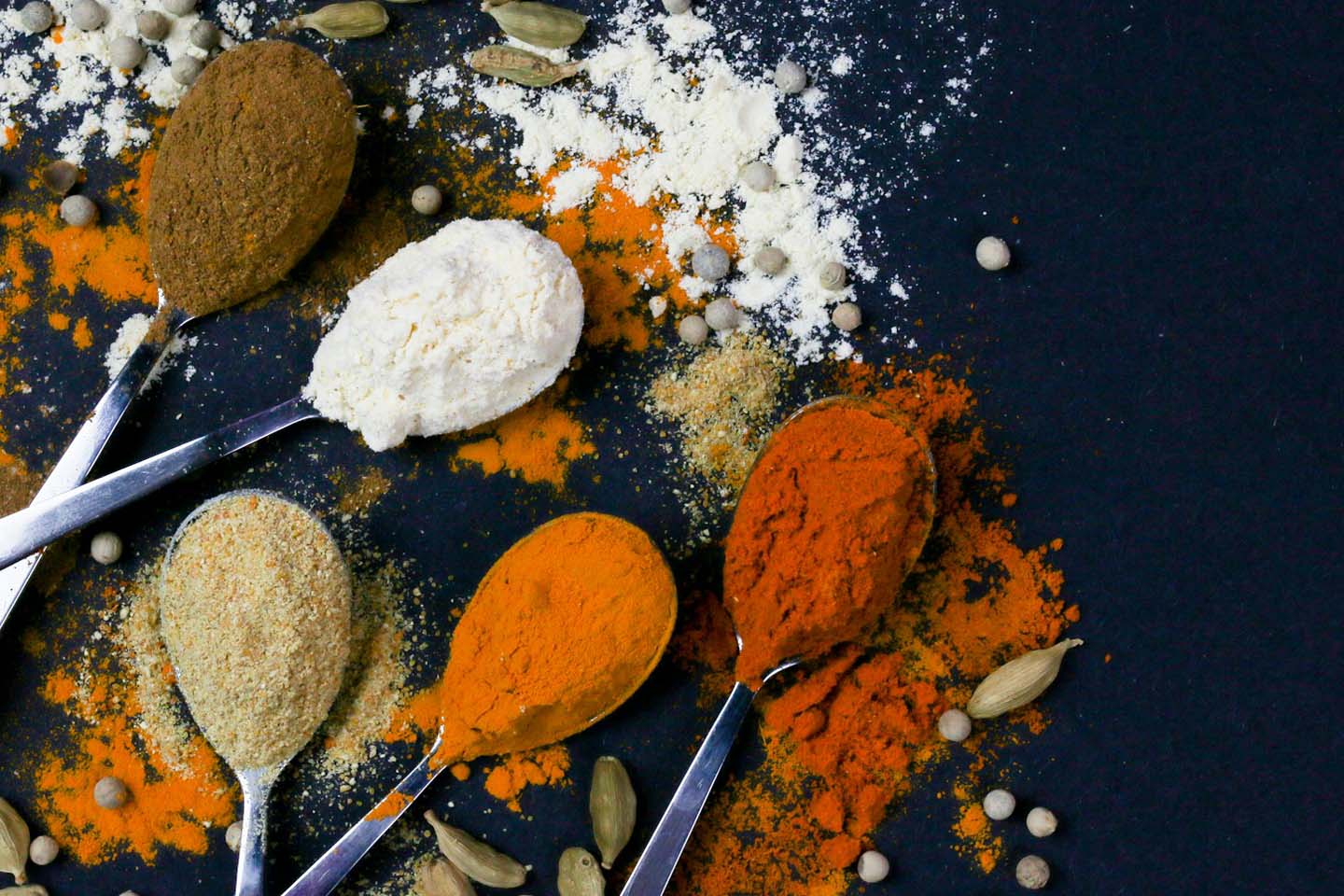 spoons holding colorful spices on a black background