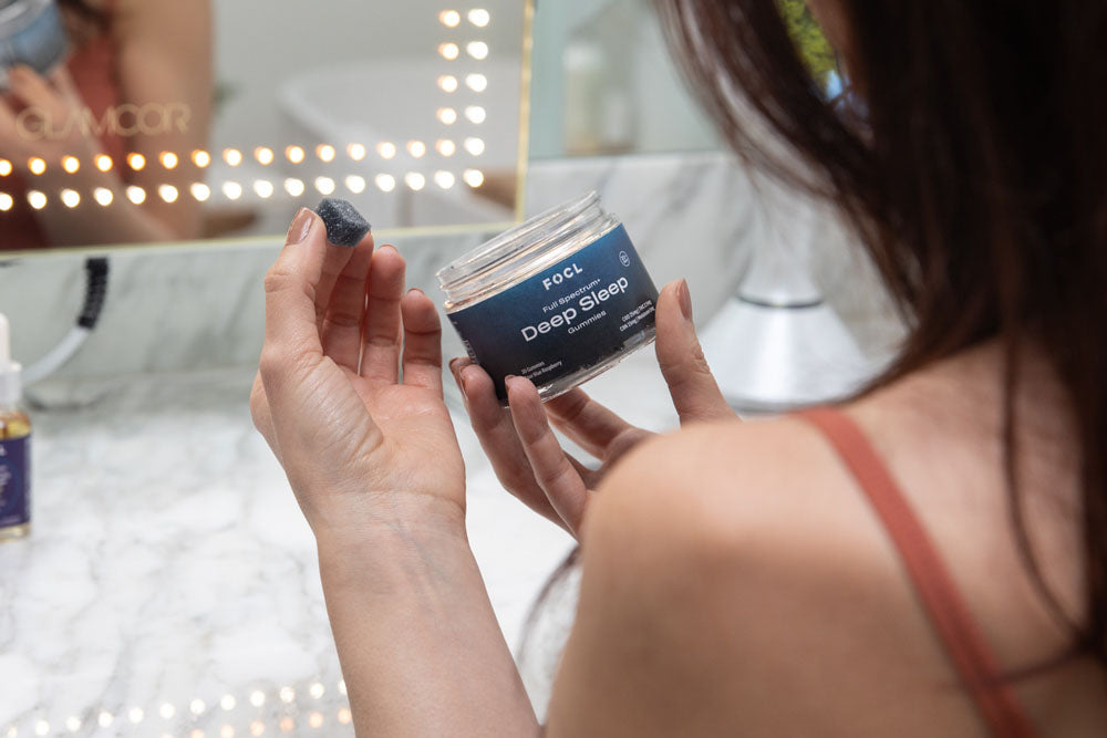 woman taking a blue CBD gummy from a FOCL Deep Sleep jar in front of a mirror