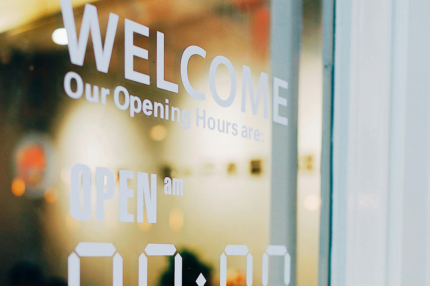 a close-up photo of a store's glass door printed with welcome sign and opening hours