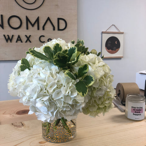 Nomad Candle Studio - white flowers in front of wood sign with Nomad logo