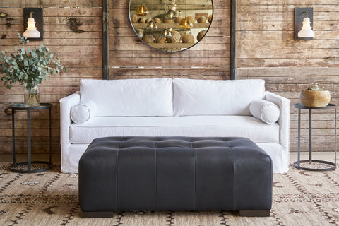 White sofa in front of a wood wall with a round mirror. Black leather bench in front. Photographed in Bracco Black.