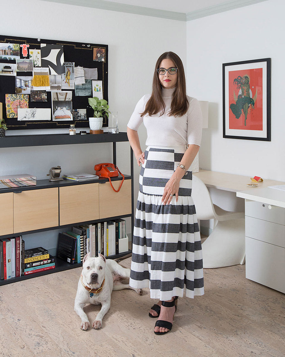 interior portrait of Melinda Mandell standing with her dog laying by her feet