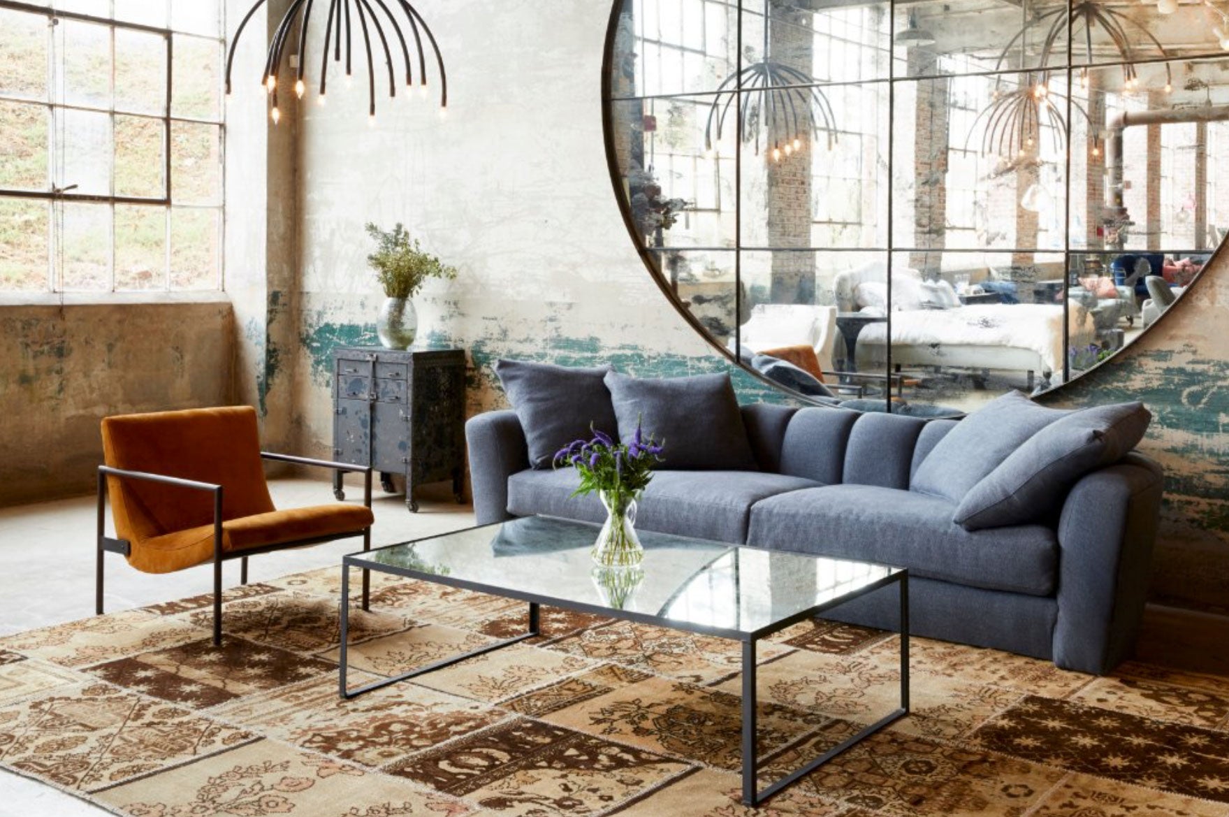 Light filled Interior building with a blue sofa and brown chair and large round mirror on the wall