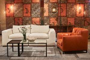  Richard chair in Dawson Rust next to a light sofa and a glass coffee table. In the background is a patterned red wall. There is also a floor lamp behind the sofa. 