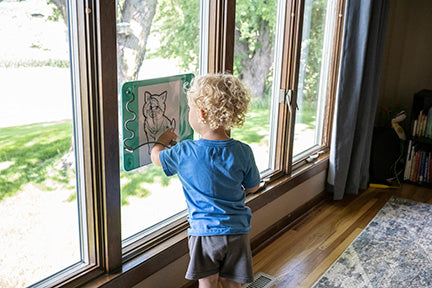 Toddler drawing on a Busy Baby Toddler Mat attached to a window.