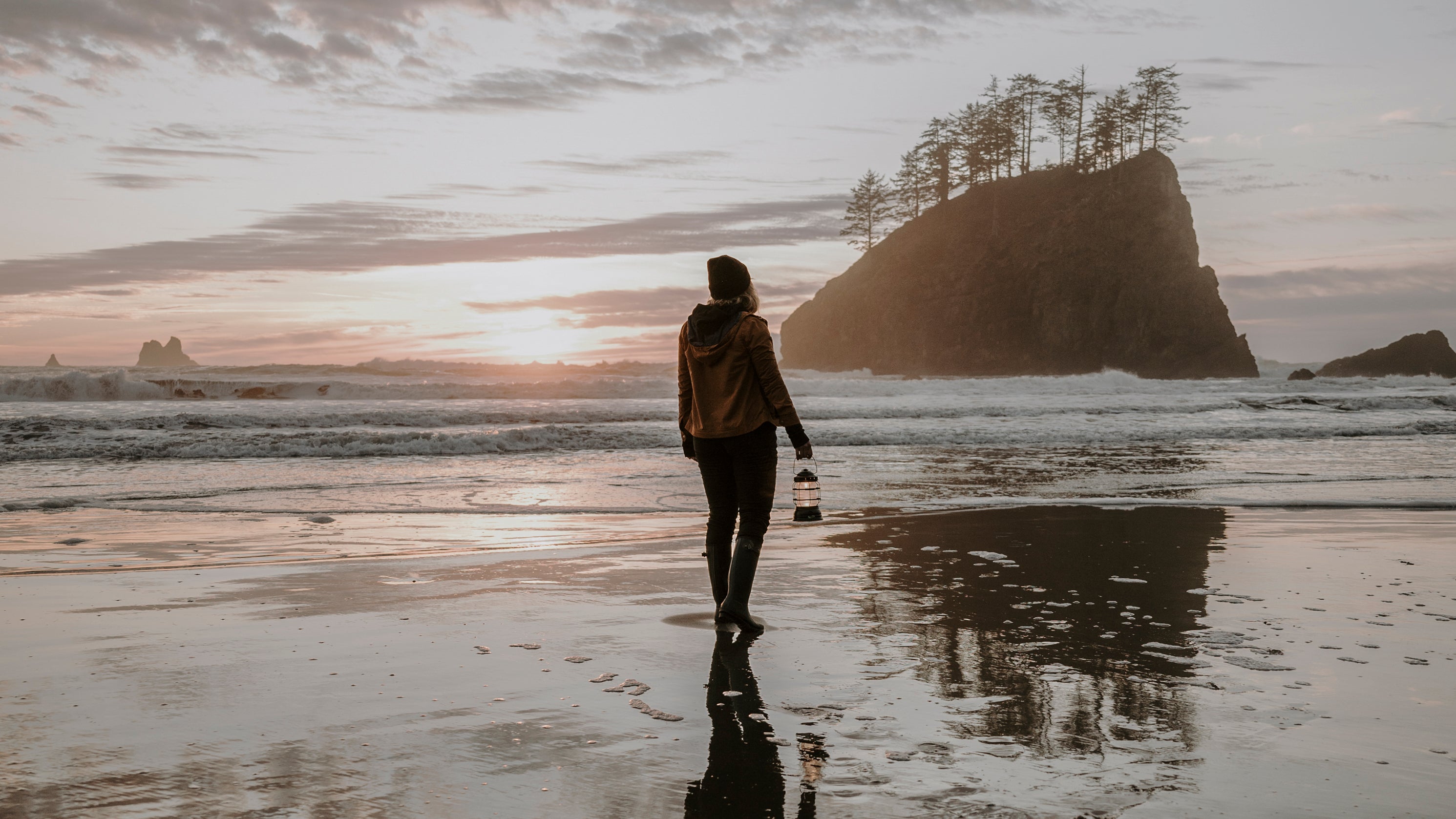 Person on a beach with a lantern watching the sunset