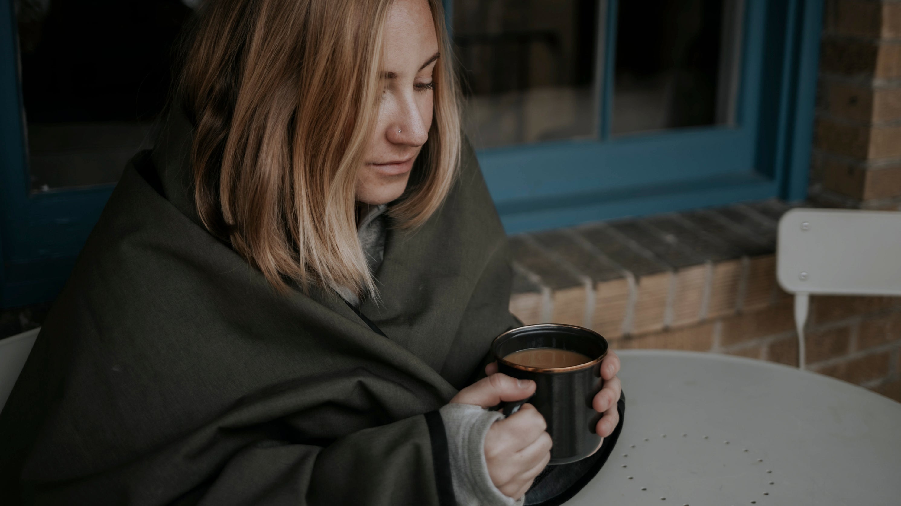 Women wrapped in a blanket sitting outside holding a warm drink