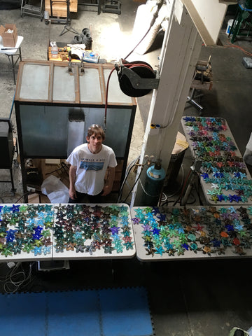 John Gibbons de pie en su estudio mirando hacia arriba rodeado de cientos de coloridas estrellas de mar de cristal sobre las mesas.