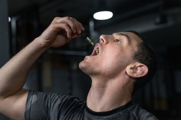 A man in a black shirt taking CBD oil from a tincture