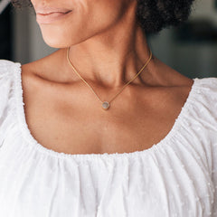 A close-up, cropped photo of Close By Me Jewelry's 8mm Sliding Solitaire Cremation Necklace in 14K Yellow Gold being worn.