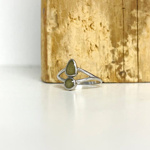 Close By Me's Double-Setting Split Shank Cremation Ring in 14K White Gold set with ashes from aquamation, resting on a white surface in front of a standing wooden slab.