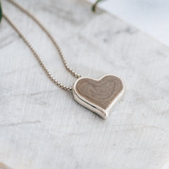 Close-up photo of Close By Me Jewelry's Tilted Heart Cremation Necklace, laying on a light grey marbled surface.