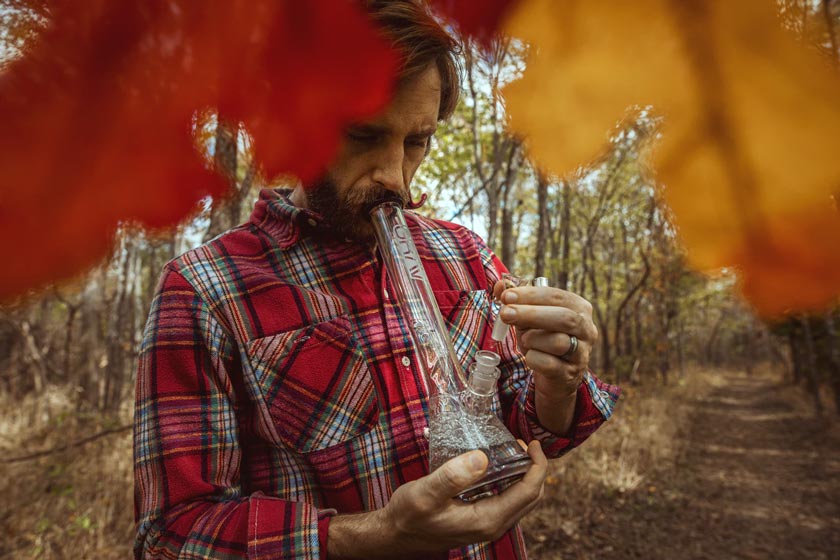 Man smoking from a glass bong in a forest