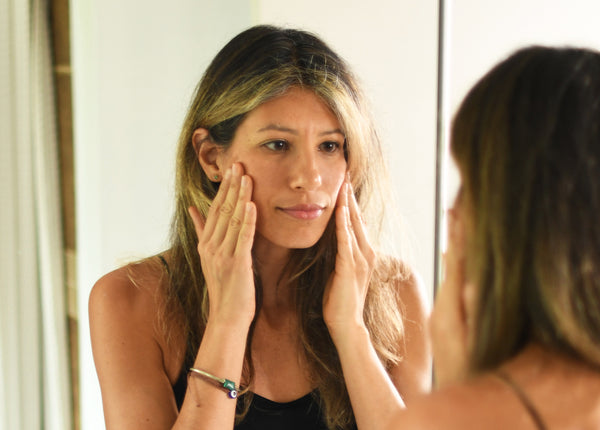 Woman looking in mirror with hands on face 