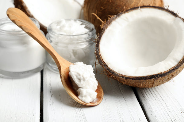 Raw Coconut Oil on wooden spoon next to fresh coconut