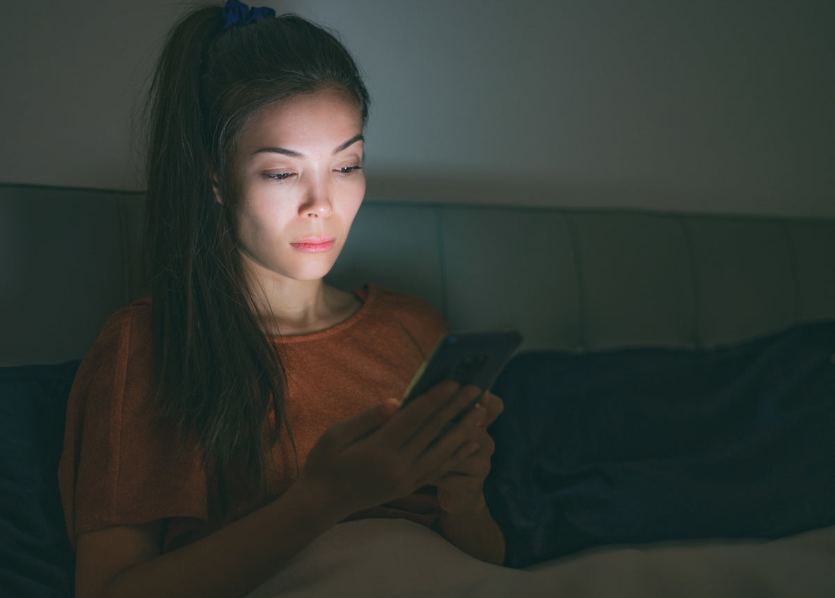 woman looks at smart phone on bed