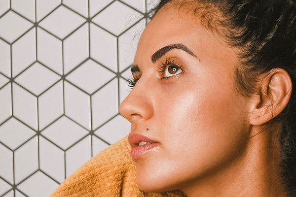 Woman cleansing her face with a towel against white tiled wall