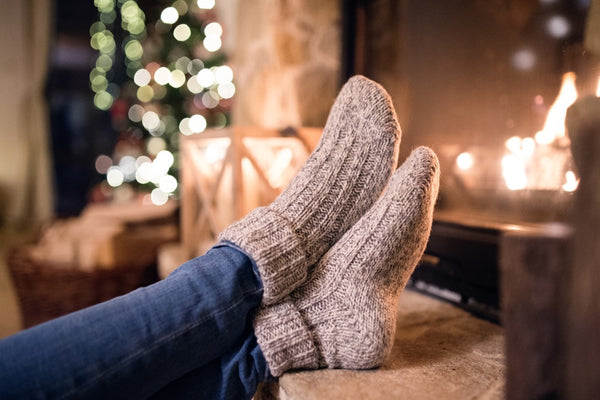 Woman in cozy socks in front of fireplace with holiday lights in the background