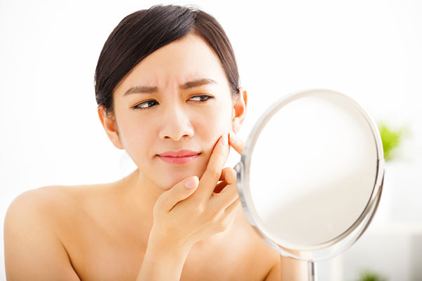 Brunette woman looking into a magnifying mirror examining her skin