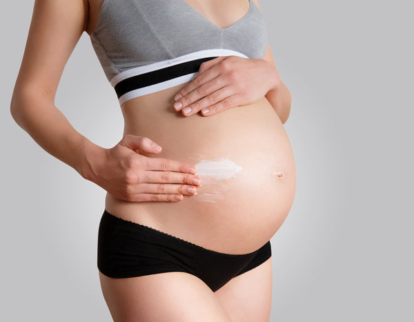 woman rubbing cream on pregnant belly