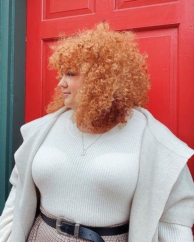 A white woman with tight red curls in front of a red door