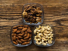 walnuts, almonds, and cashews in bowls on wooden table