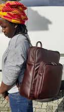 Load image into Gallery viewer, A beautiful African lady carrying a beautiful genuine leather backpack in dard tan from Cape Masai Leather. 
