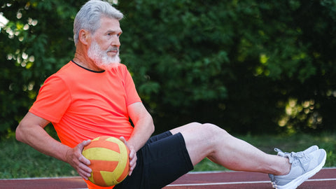 Older Man With Grey Hair Sitting on Running Track Lifting Medicine Ball