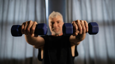 Older Man With Grey Hair Holding Two Dumbbells Towards The Camera 