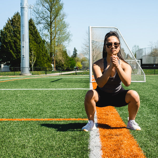 woman does a deep squat knee bend on soccer field — GRIT Superfoods