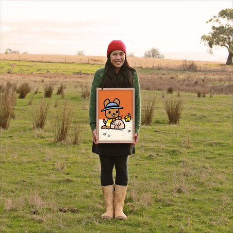 Roobee Roo artist holding print in country setting.