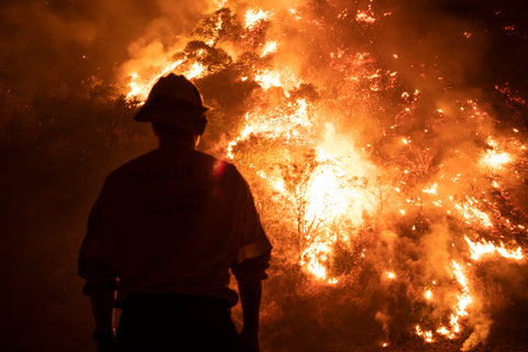 Firefighter standing in front of a massive wildfire.