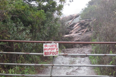 A sign that says "Private Property Keep Out" with evidence of a mudslide behind it.