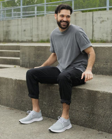 Image of a man sitting on a cement step comfortably wearing Vessi waterproof shoes