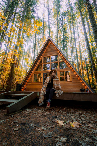 Woman wrapped up in a blanket sitting on a cabin patio in the fall.