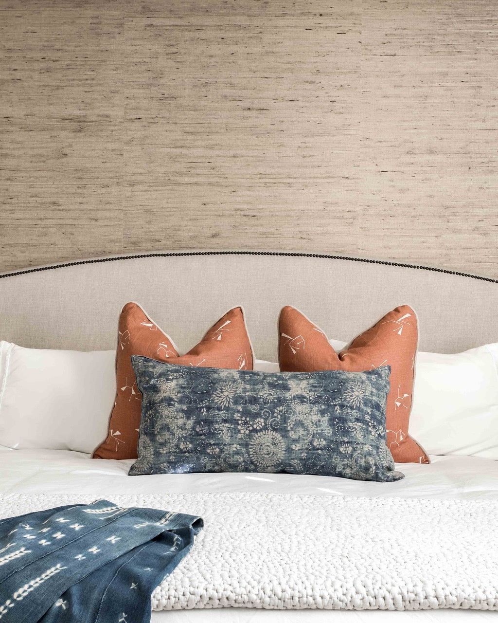 Detailed view of a bed with two earth toned pillows and a natural grasscloth on the wall behind