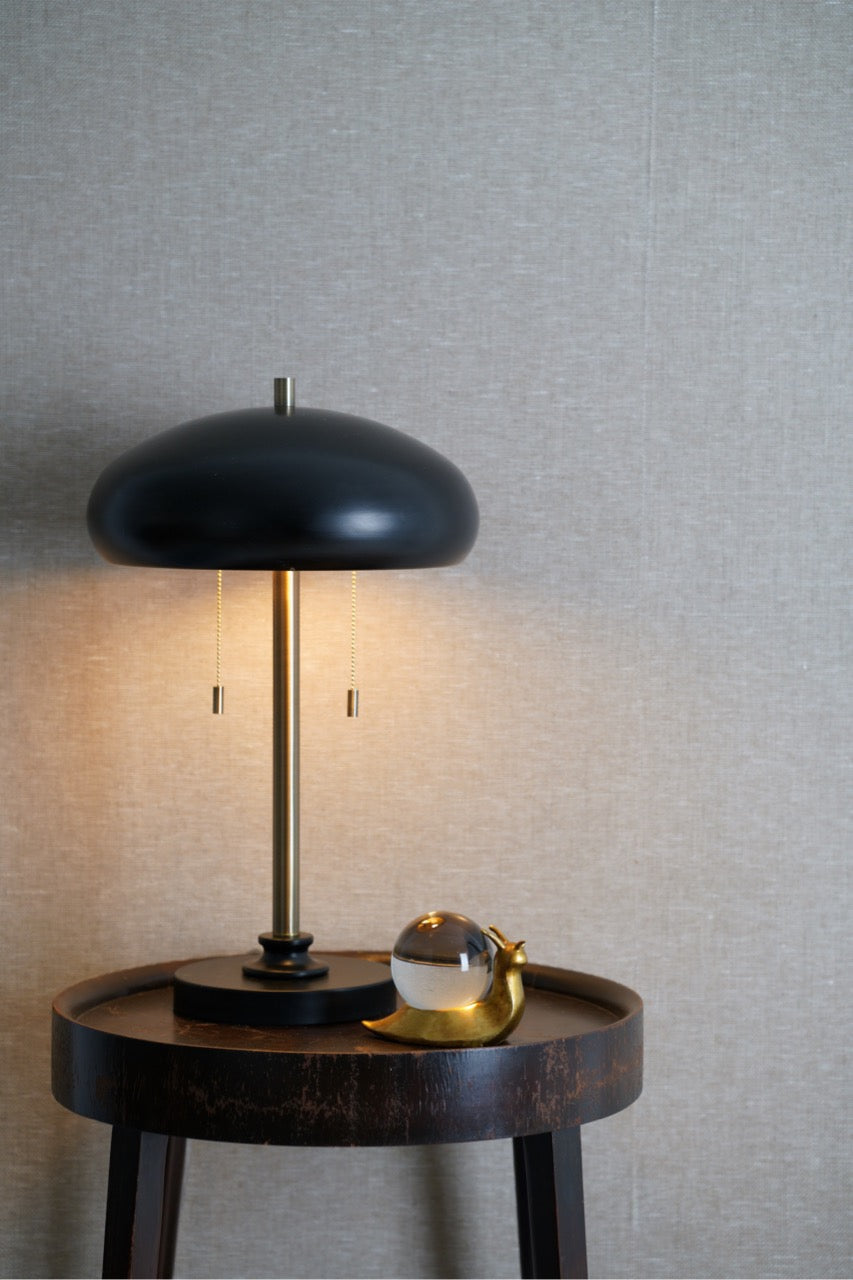 Warmly lit black table lamp on a small round table with a glass snail decorative object